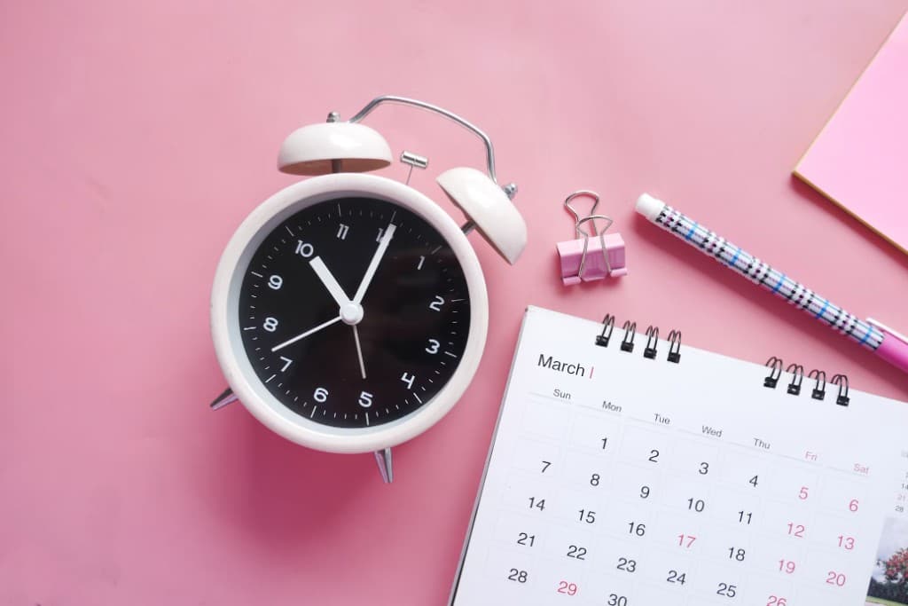 Alarm clock and March calendar on a pink desk