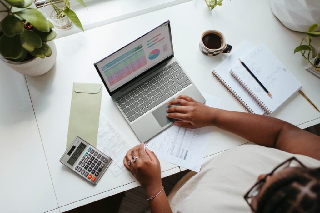 Person working on a laptop with a calculator and budget spreadsheet